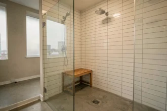 Coin douche dans un studio avec paroi en verre frameless, carrelage métro blanc et sol en béton poli