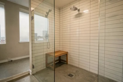 Coin douche dans un studio avec paroi en verre frameless, carrelage métro blanc et sol en béton poli