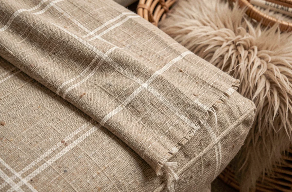 Détail en gros plan de la texture du tissu lin lavé beige d'un plaid posé sur un coussin de canapé
