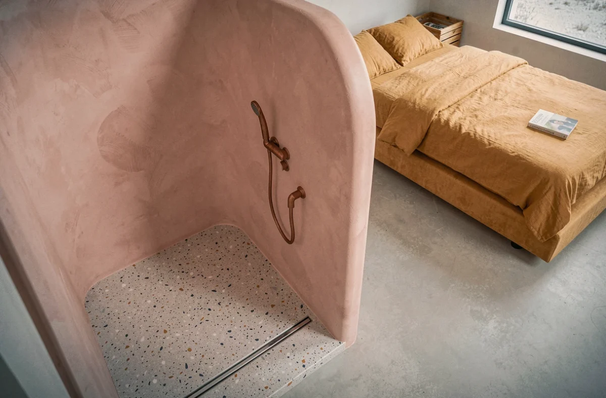 Vue plongeante d'un wet room en micro-béton rose dans un studio avec séparation demi-cloison et lit plateforme
